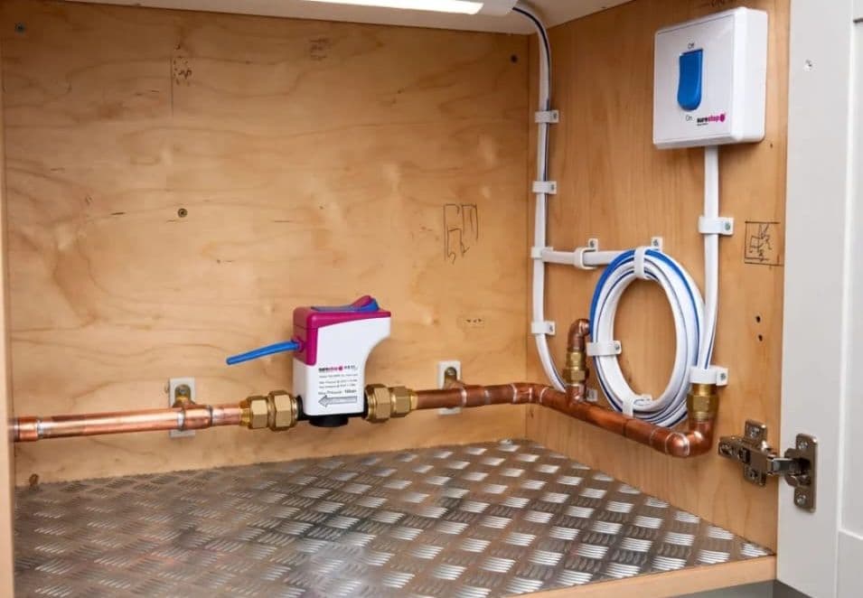 Metered water pipework and stopcock installed inside a kitchen cabinet